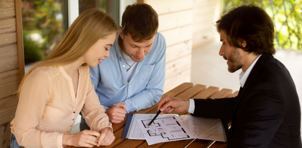 Couple reviewing architectural floor plans with a real estate agent, discussing layout and features that impact future real estate value during a home-buying consultation