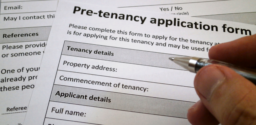 Close-up of a hand filling out a pre-tenancy application form, focusing on sections for tenancy and applicant details