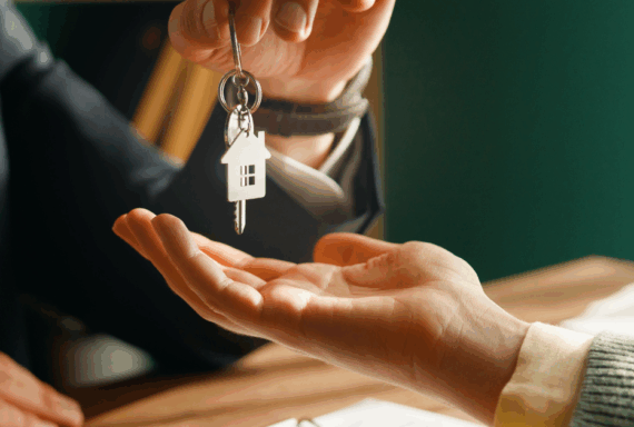 Person handing house-shaped key to another during a real estate transaction