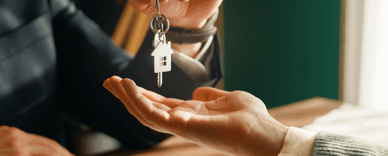 Person handing house-shaped key to another during a real estate transaction