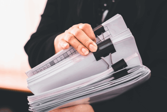 Person in business attire holds thick stack of clipped documents and case files