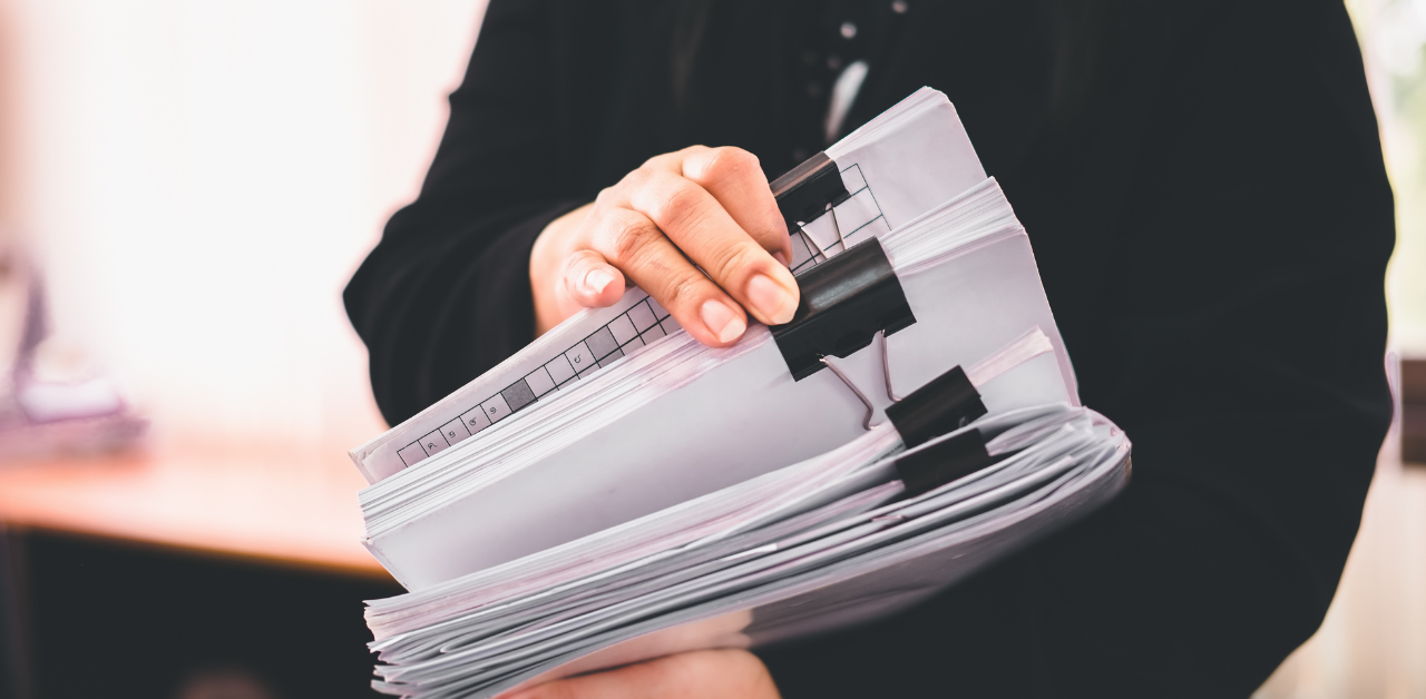 Person in business attire holds thick stack of clipped documents and case files