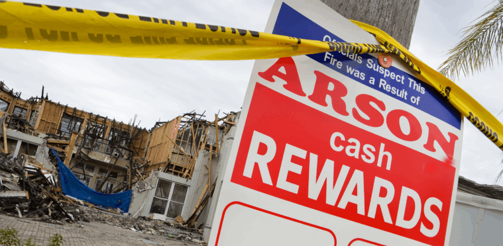 Property Management Burned apartment complex behind arson reward sign with police tape and partial structural collapse