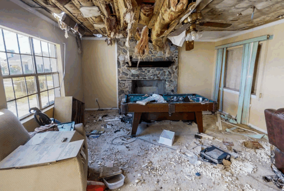 Property Management, Real Estate Severely damaged living room with ceiling insulation hanging down, debris on floor, and ruined furniture