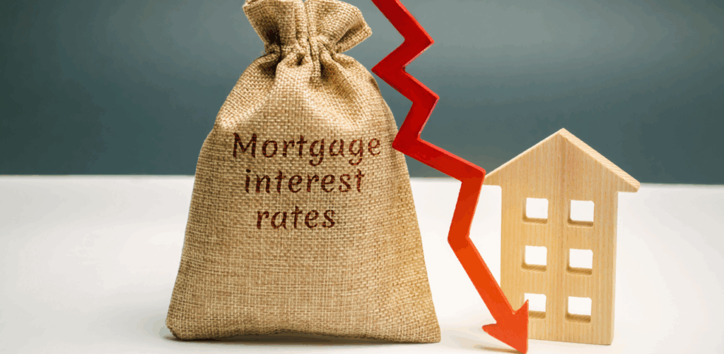 Bag labeled “mortgage interest rates” with red arrow pointing down beside a wooden house
