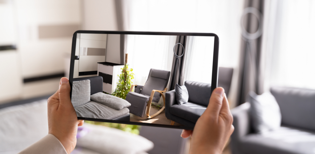 Hands holding a tablet showing a virtual view of a furnished living room, blending with the actual room in the background