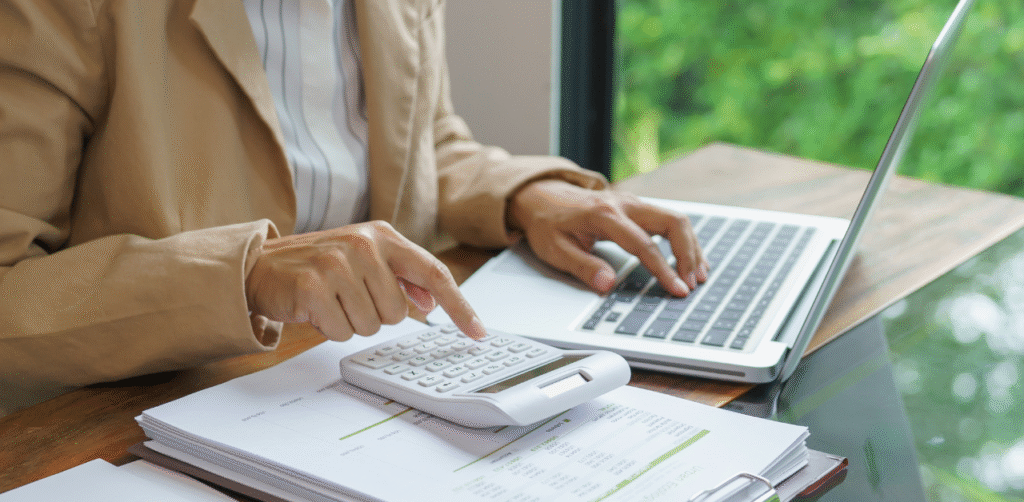 Person using calculator and laptop to review rental expenses and budget, showing financial planning for housing