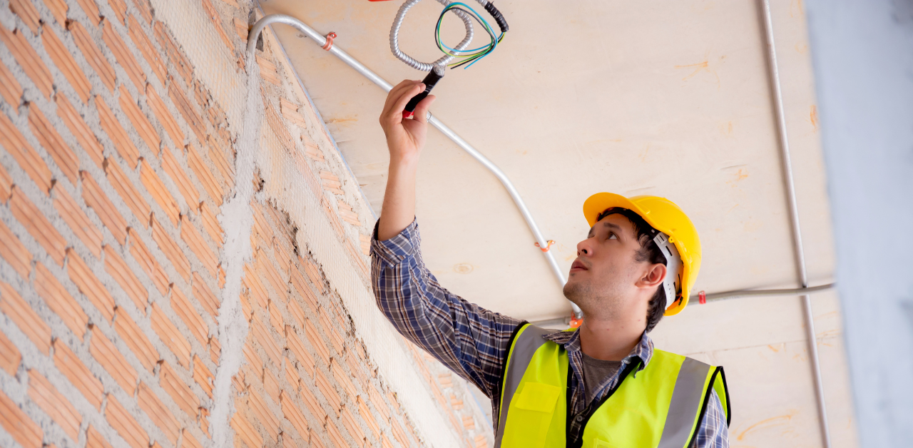 Electrician in hard hat installing wiring through ceiling conduit, highlighting professional electrical services