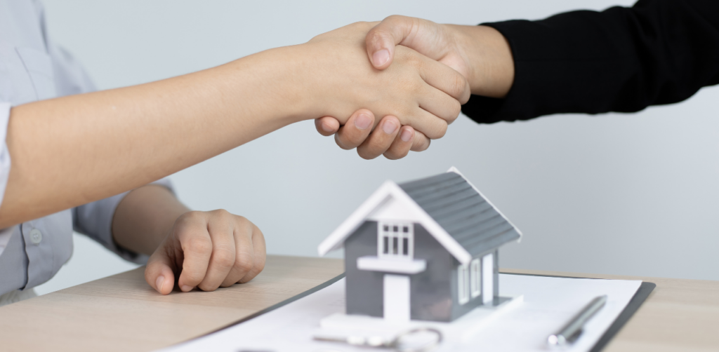 Landlord and tenant shaking hands over rental agreement with house model
