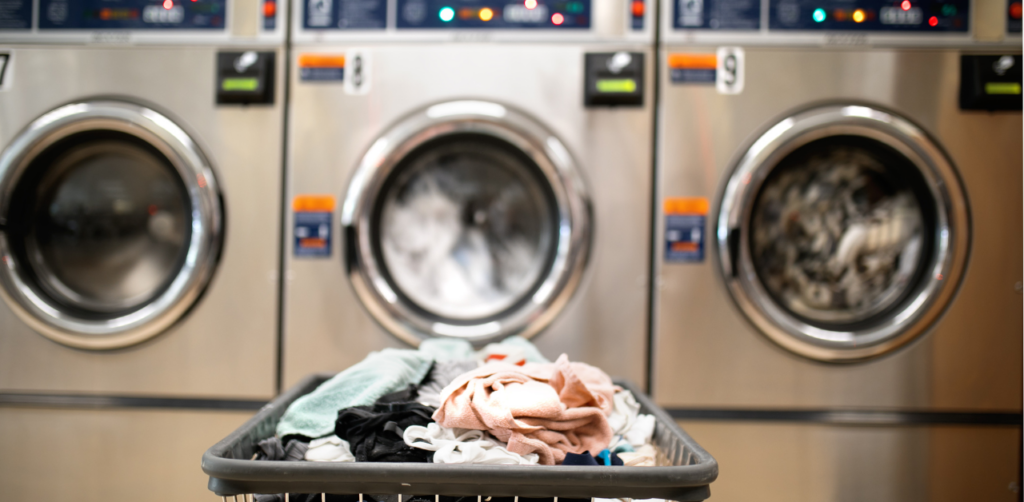 Laundry cart filled with clothes in front of industrial washing machines at a laundromat