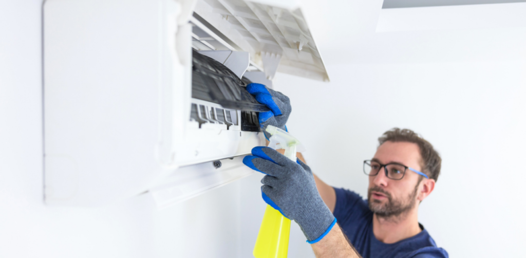 Technician cleaning an indoor air conditioner filter with spray solution during home HVAC maintenance service