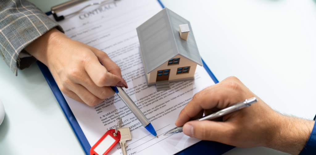 Close-up of hands signing a real estate contract with a model house and house keys placed on the document