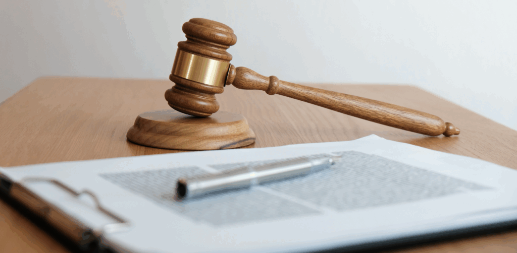 Wooden judge’s gavel rests beside a legal document and pen on a table, symbolizing a courtroom ruling or legal judgment