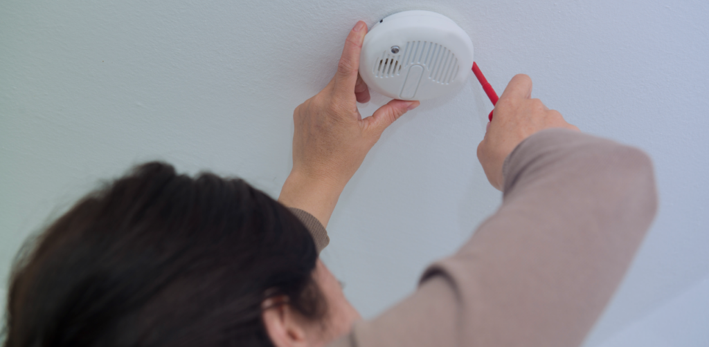 Person uses a screwdriver while installing or inspecting a smoke detector on a ceiling