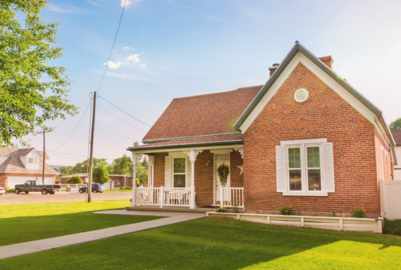 Red brick house with a front porch and neatly maintained lawn on a sunny residential street