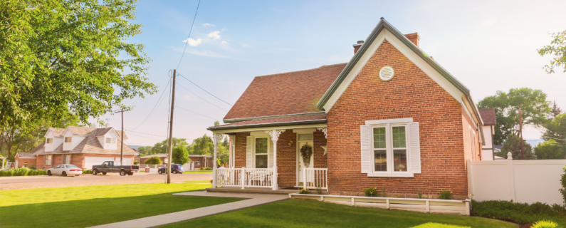 Red brick house with a front porch and neatly maintained lawn on a sunny residential street