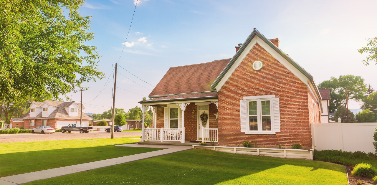 Red brick house with a front porch and neatly maintained lawn on a sunny residential street