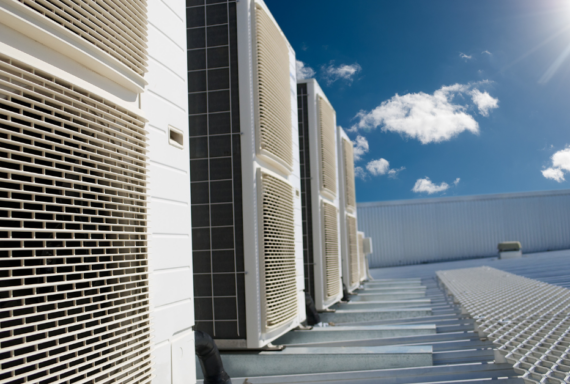 Rooftop HVAC units with metal grilles under a bright blue sky with scattered clouds