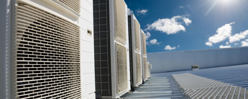 Rooftop HVAC units with metal grilles under a bright blue sky with scattered clouds