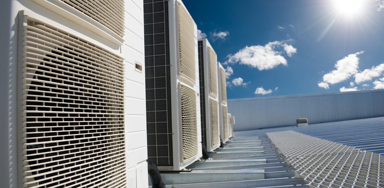 Rooftop HVAC units with metal grilles under a bright blue sky with scattered clouds