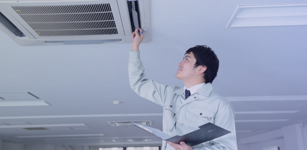 Technician inspects a ceiling-mounted air conditioning unit with a clipboard
