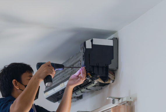 Technician repairs a wall-mounted air conditioner using a power drill