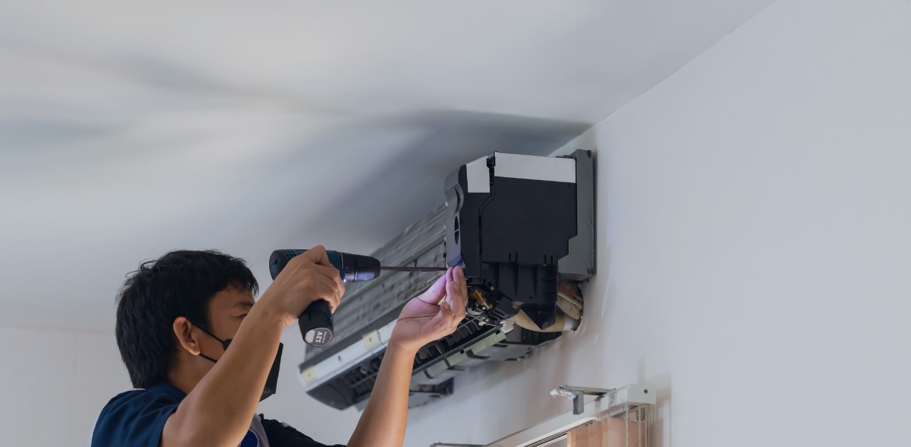 Technician repairs a wall-mounted air conditioner using a power drill
