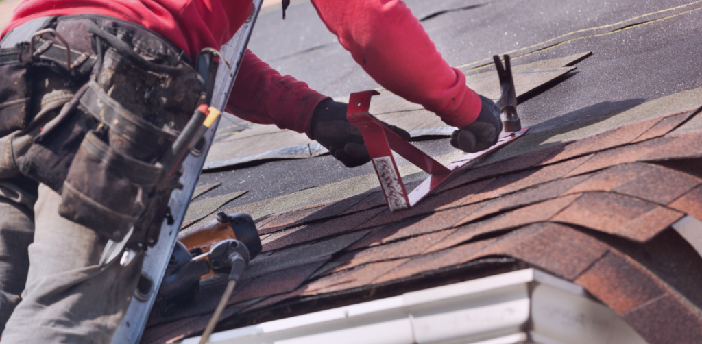 Roofer in work gear using roofing tools to install or repair asphalt shingles on a residential roof