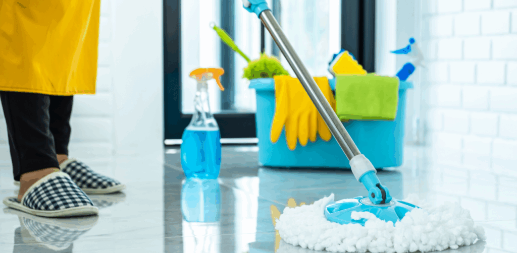 Person mopping a shiny tile floor with cleaning supplies and gloves in the background