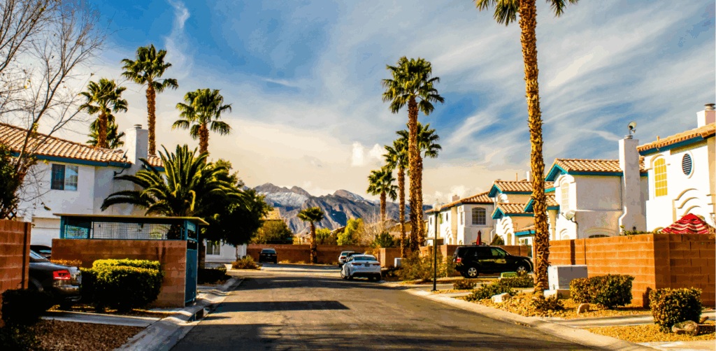 Sunny suburban street in Las Vegas lined with palm trees, white houses, and distant mountains