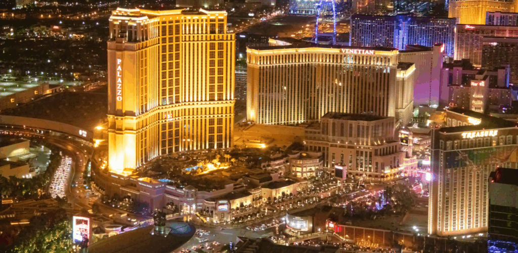 Glowing aerial night view of the Las Vegas Strip featuring iconic resorts like The Palazzo, Venetian, and Treasure Island, bustling with lights and traffic