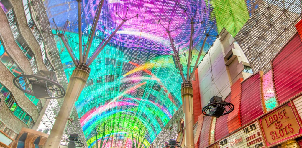 Colorful LED canopy display above a busy street with shops, including a sign for Loose Slots, in a lively entertainment district