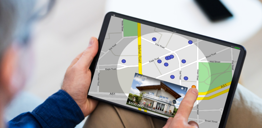 Person holding a tablet displaying a real estate map with property locations and a listing detail popup showing a house for sale