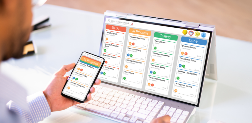 Person using a phone and laptop showing a task management app with columns labeled To Do, In Progress, Testing, and Done