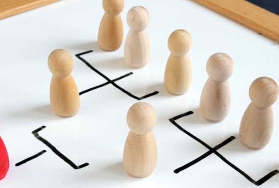 Wooden figurines on a whiteboard depicting an organizational chart, with a red figure representing leadership or management