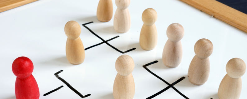 Wooden figurines on a whiteboard depicting an organizational chart, with a red figure representing leadership or management