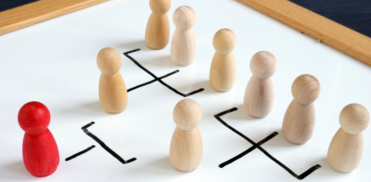 Wooden figurines on a whiteboard depicting an organizational chart, with a red figure representing leadership or management