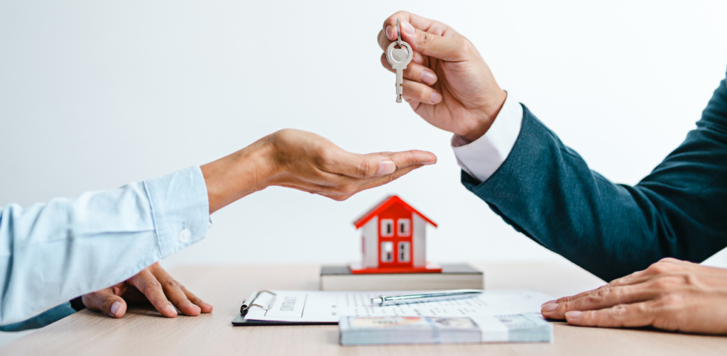 Property Management Real estate agent handing house keys to a buyer, with documents and a small house model on a table