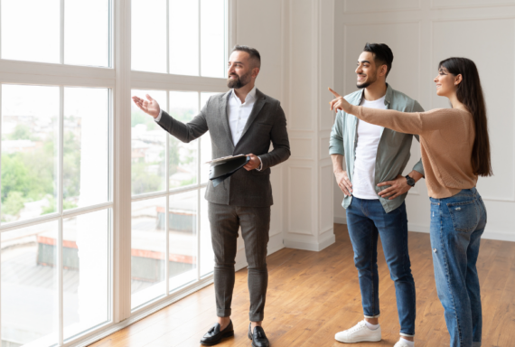 Smiling couple touring a modern home with a real estate agent, admiring the large windows