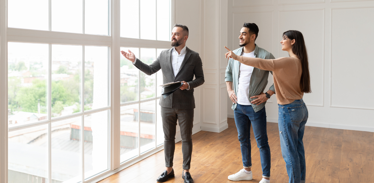 Smiling couple touring a modern home with a real estate agent, admiring the large windows