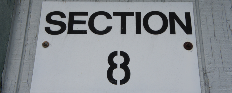 Property Management White sign labeled 'Section 8' mounted on a wall, referencing a federal housing assistance program for low-income renters