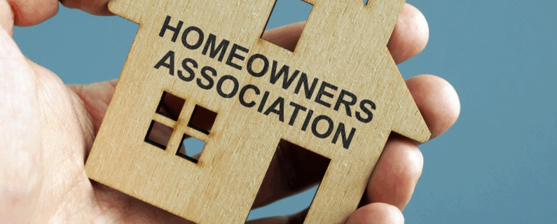 Property Management Wooden house cutout labeled Homeowners Association held in a person's hand