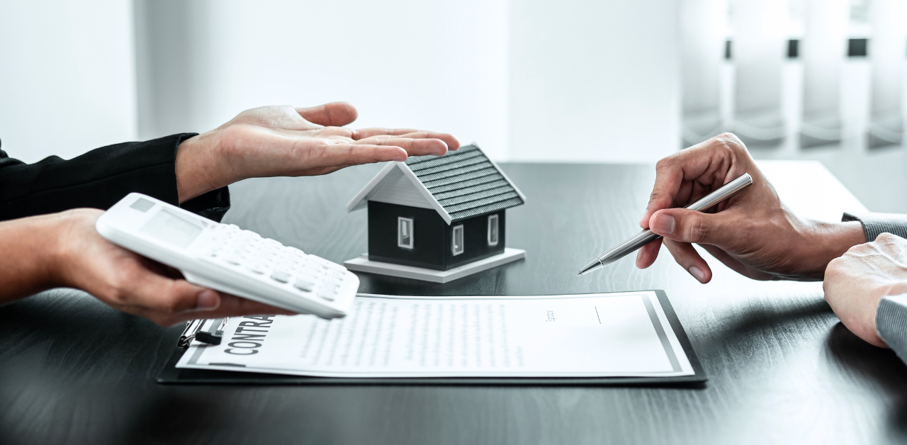 Hands discussing a real estate contract with calculator and house model, highlighting home buying costs and agreement