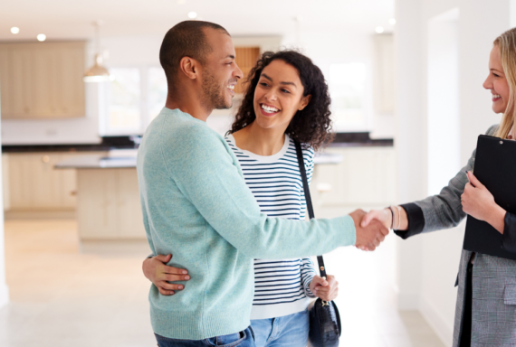 Happy couple shaking hands with real estate agent in new home, symbolizing property deal, home purchase, and agreement
