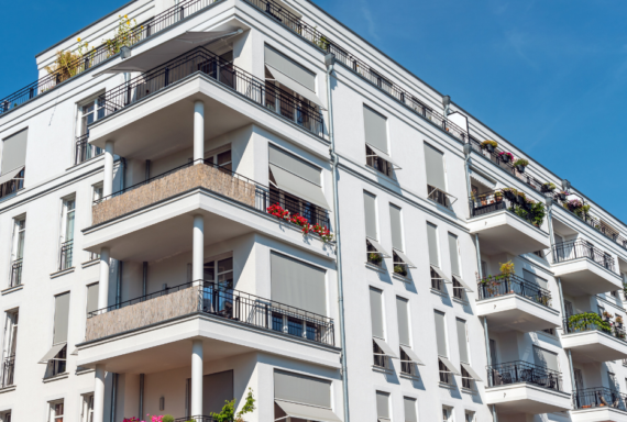 Modern apartment building with multiple balconies and large windows, showcasing urban residential real estate and contemporary housing design under a clear blue sky