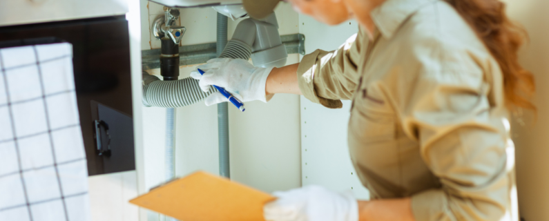 Plumber examining pipes under sink, assessing plumbing system and noting repairs on inspection checklist