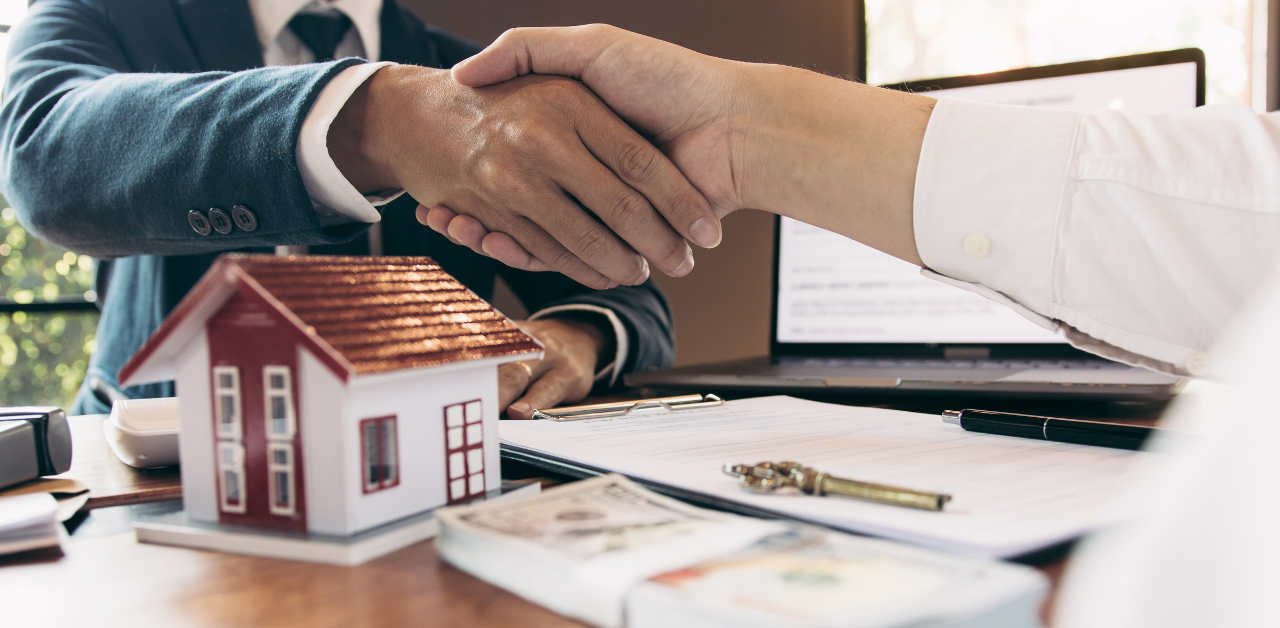 Real estate deal sealed with handshake over house model, keys, and cash, symbolizing property sale and financial agreement