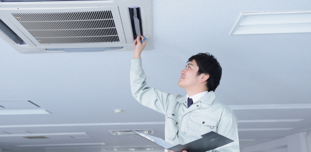 Technician inspecting ceiling air conditioner unit, performing HVAC maintenance and checking ventilation system