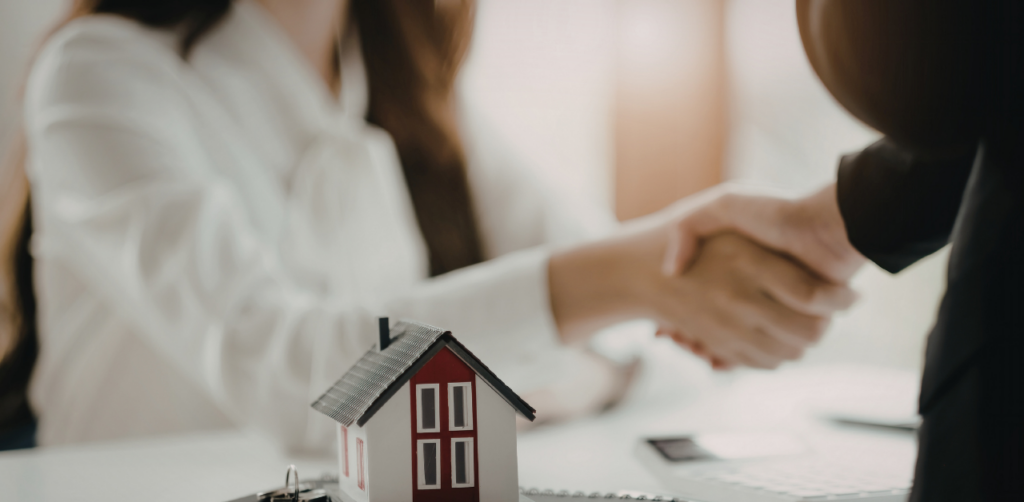 Real estate handshake over contract with house model, symbolizing property deal and home buying agreement
