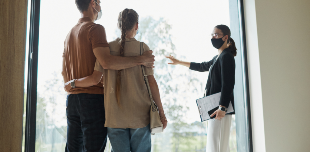 Masked real estate agent showing a home to a couple indoors, highlighting property viewing and guided house tour